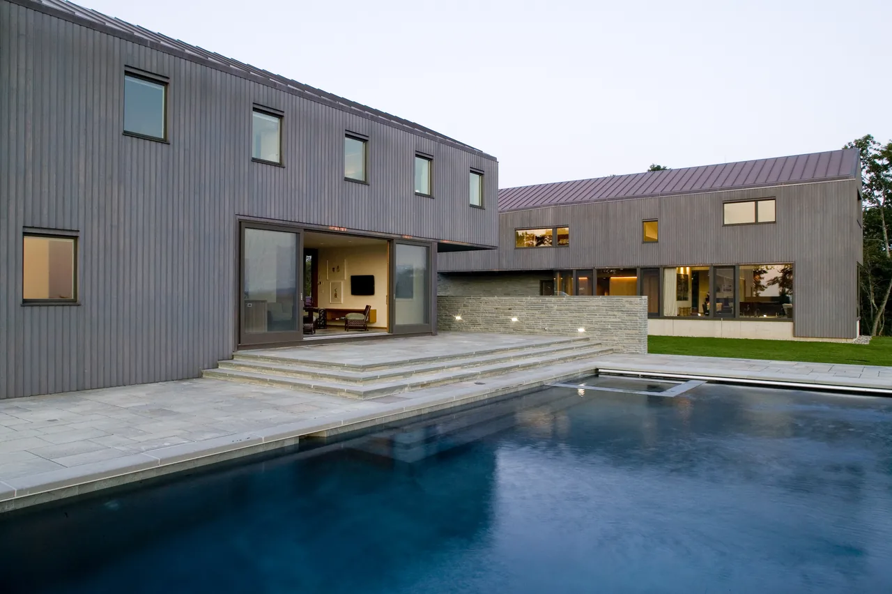 Exterior rear view of the Blue Rock House with vertical wood siding, a stone patio, and a swimming pool.