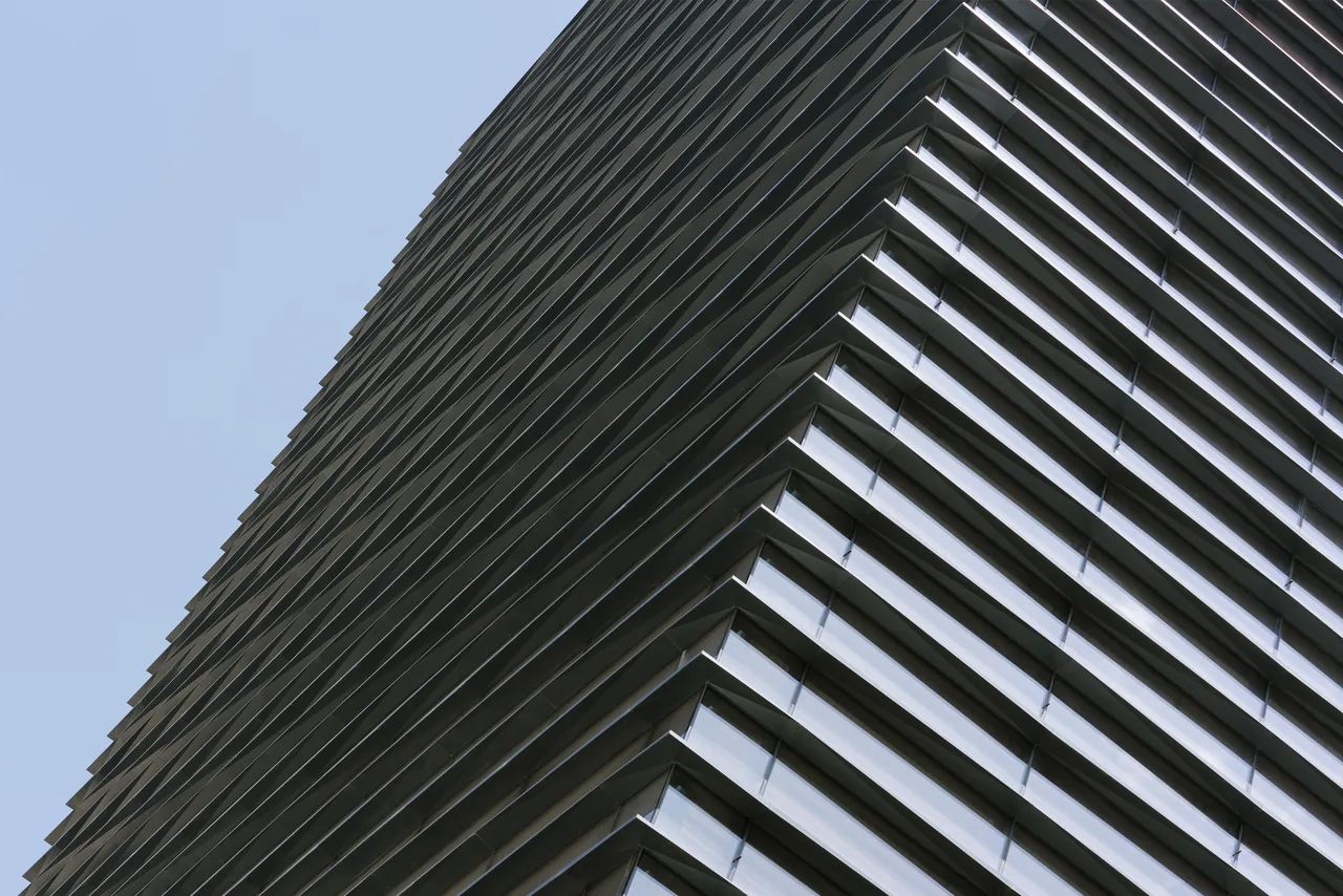 Exterior corner view of a modern building featuring horizontal metal sunshades over glass windows.