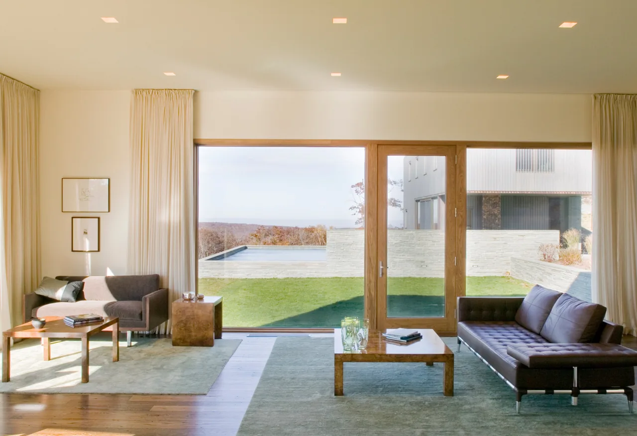 Living room with sliding glass door and floor-to-ceiling window providing a view of the pool and landscape.