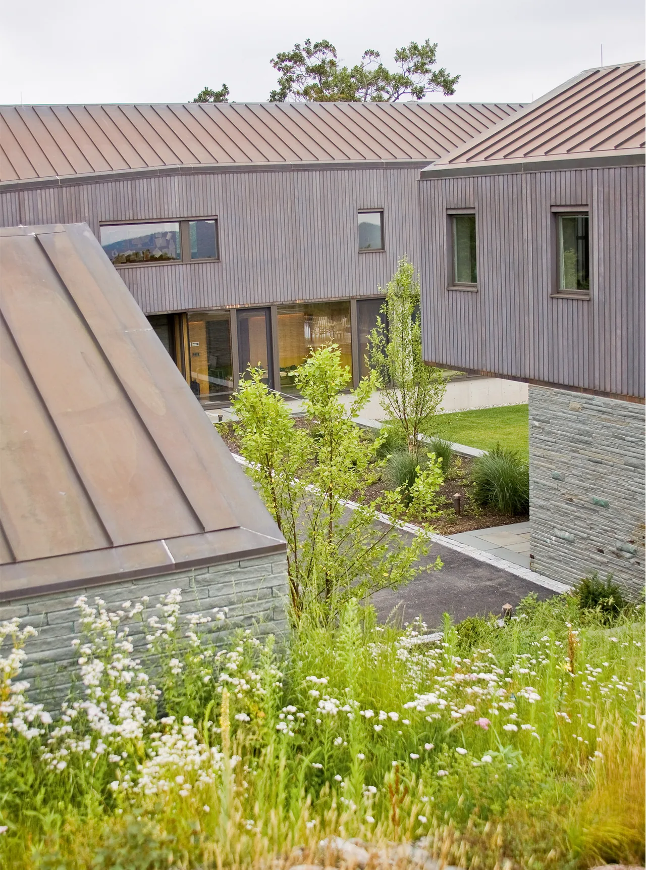 The Blue Rock House features vertical wood siding, stone retaining walls, and standing seam metal roofs in a natural landscape setting.