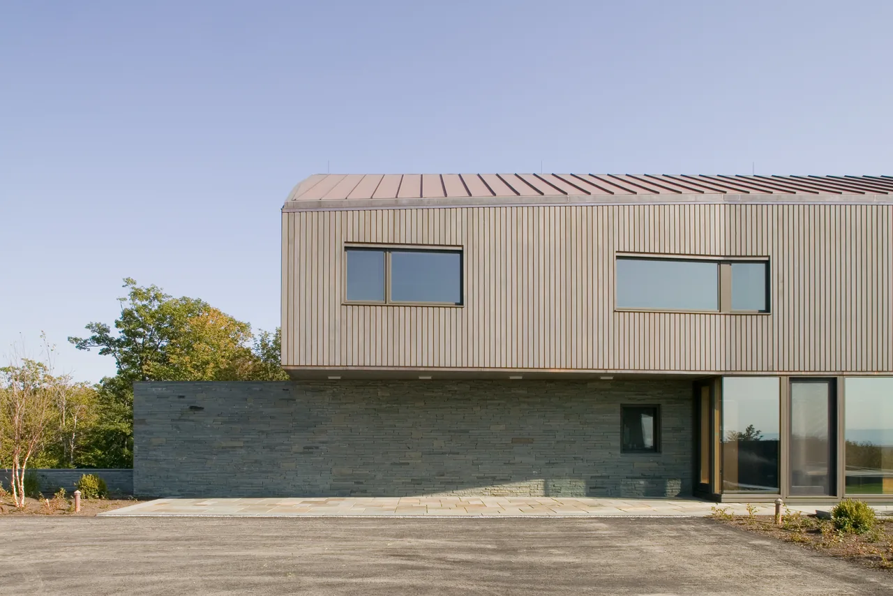The BLUE ROCK HOUSE features a modern design with wood siding above a stone base, by AW ARCH.
