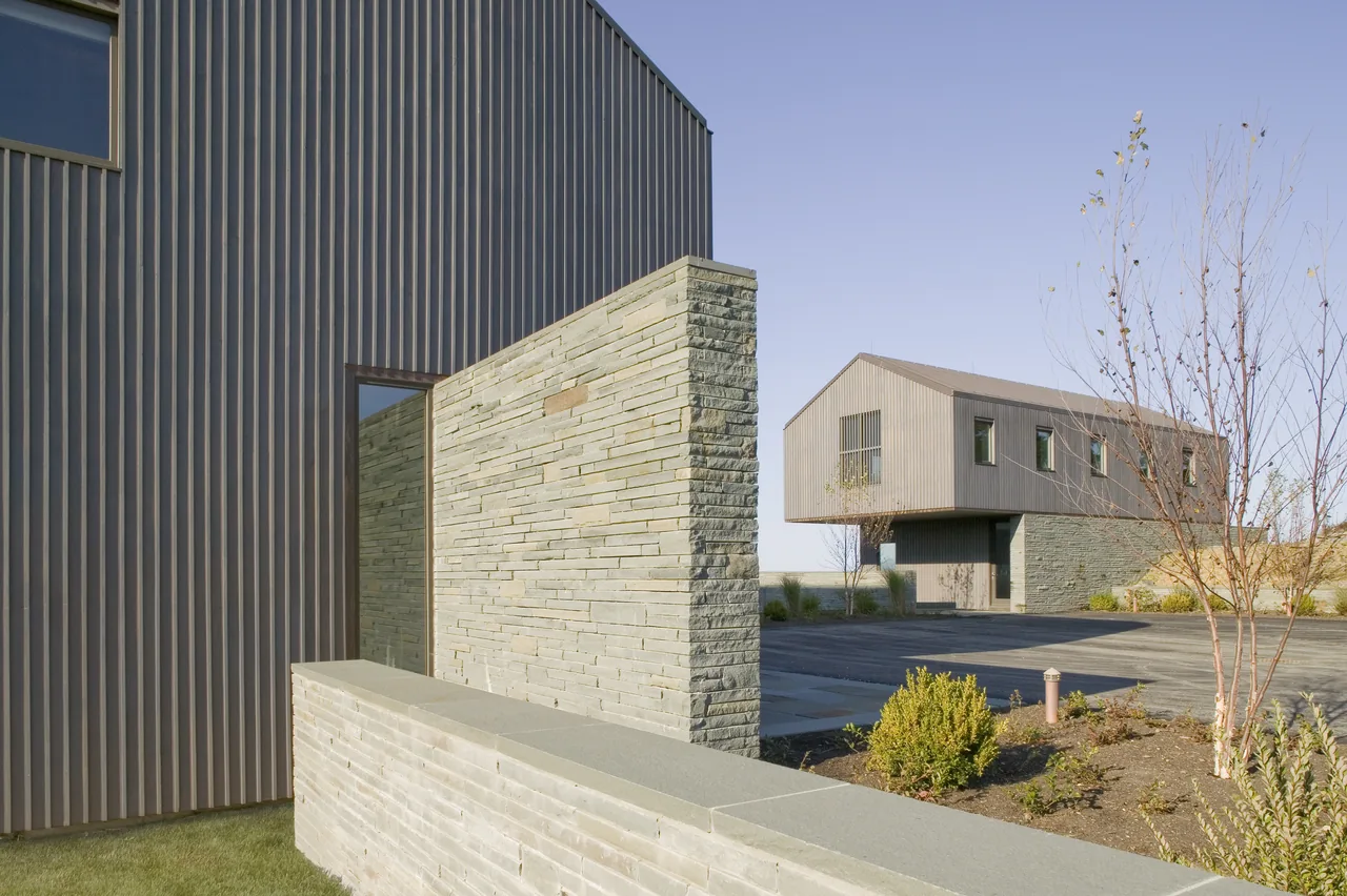 Blue Rock House features vertical metal siding and a stone retaining wall with a paved courtyard area.