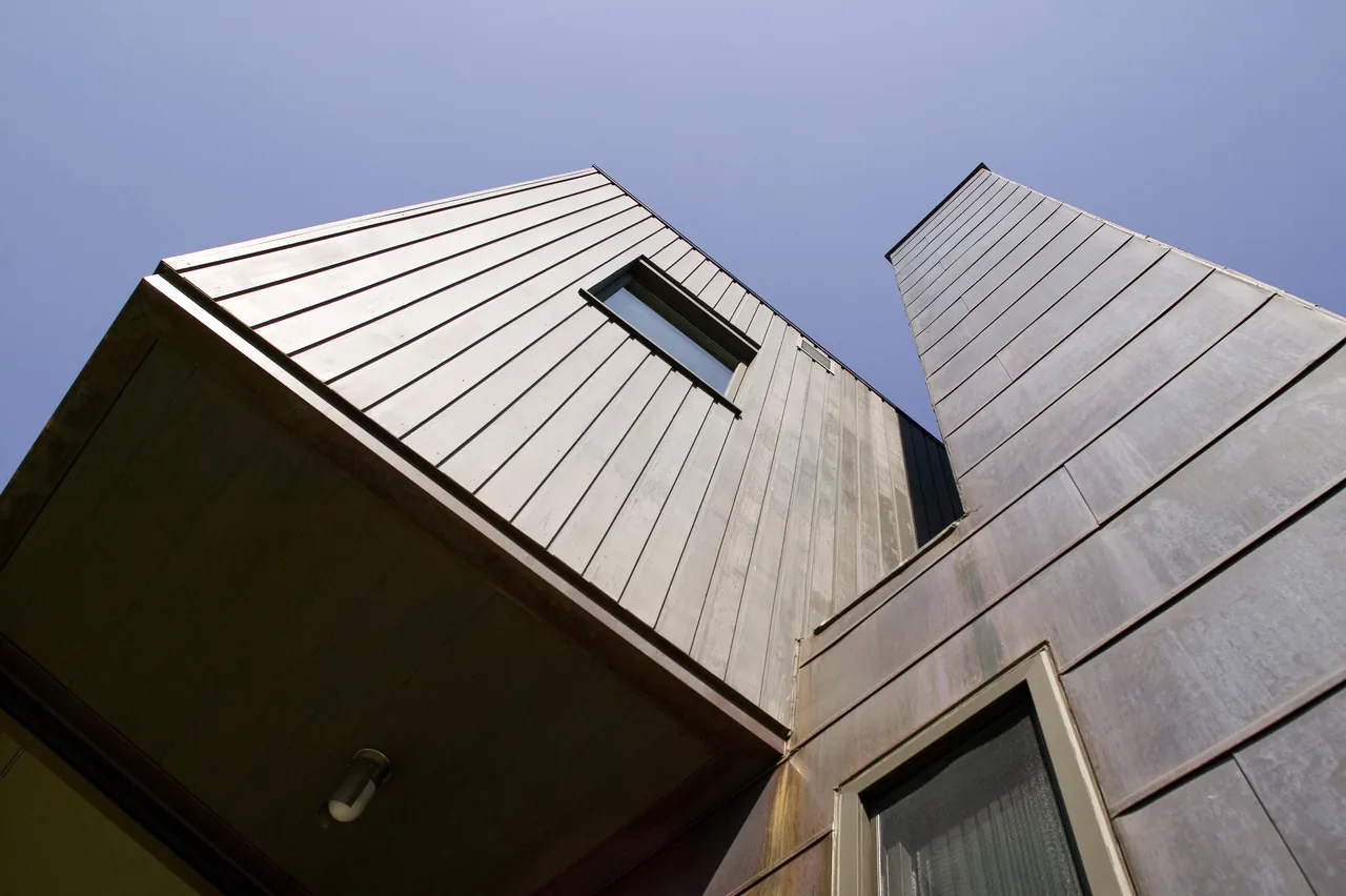 Exterior view of the BLUE ROCK HOUSE showing vertical metal siding and rectangular windows under a clear sky.