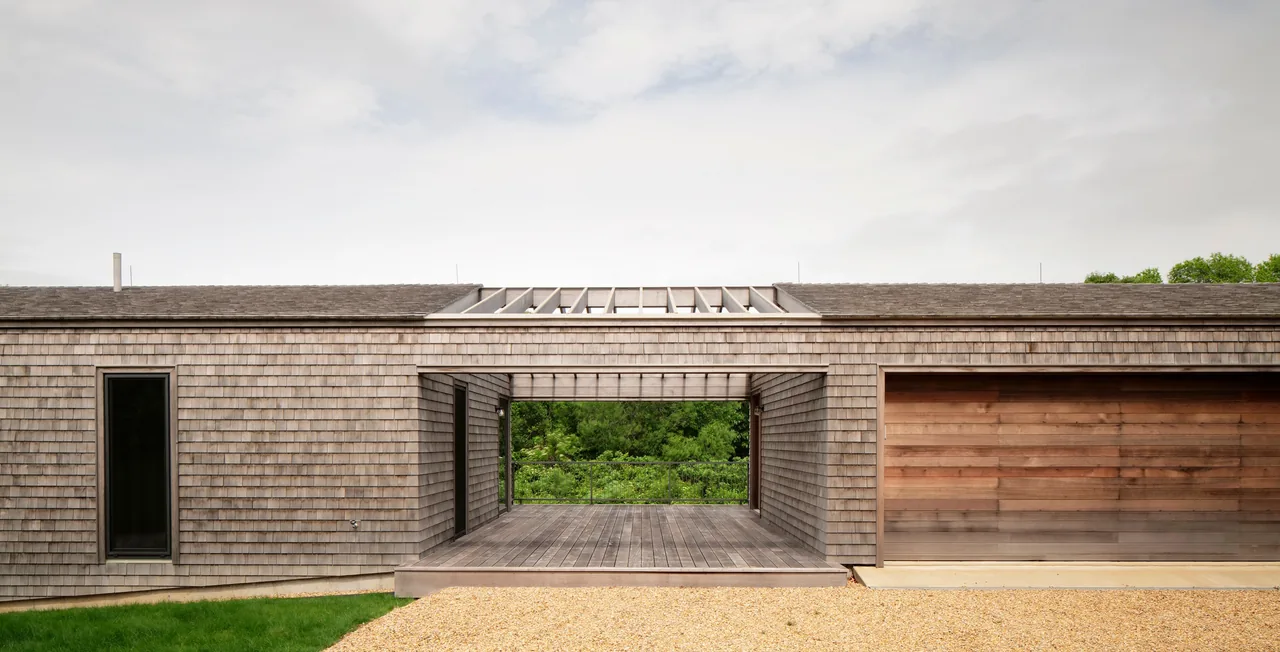 The modern Two Sheds House features wood shingle siding, a covered porch, and an attached garage with a wood door.