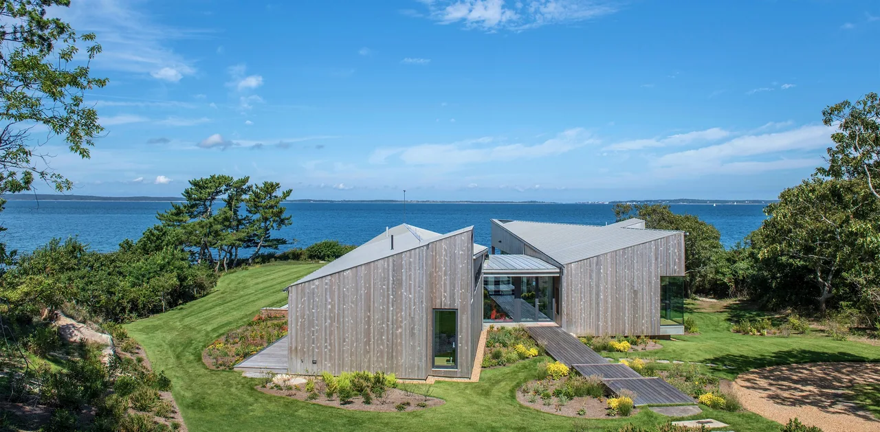 Two Sheds House at waterfront site with wood siding, two shed roofs, and a walkway leading to the water.