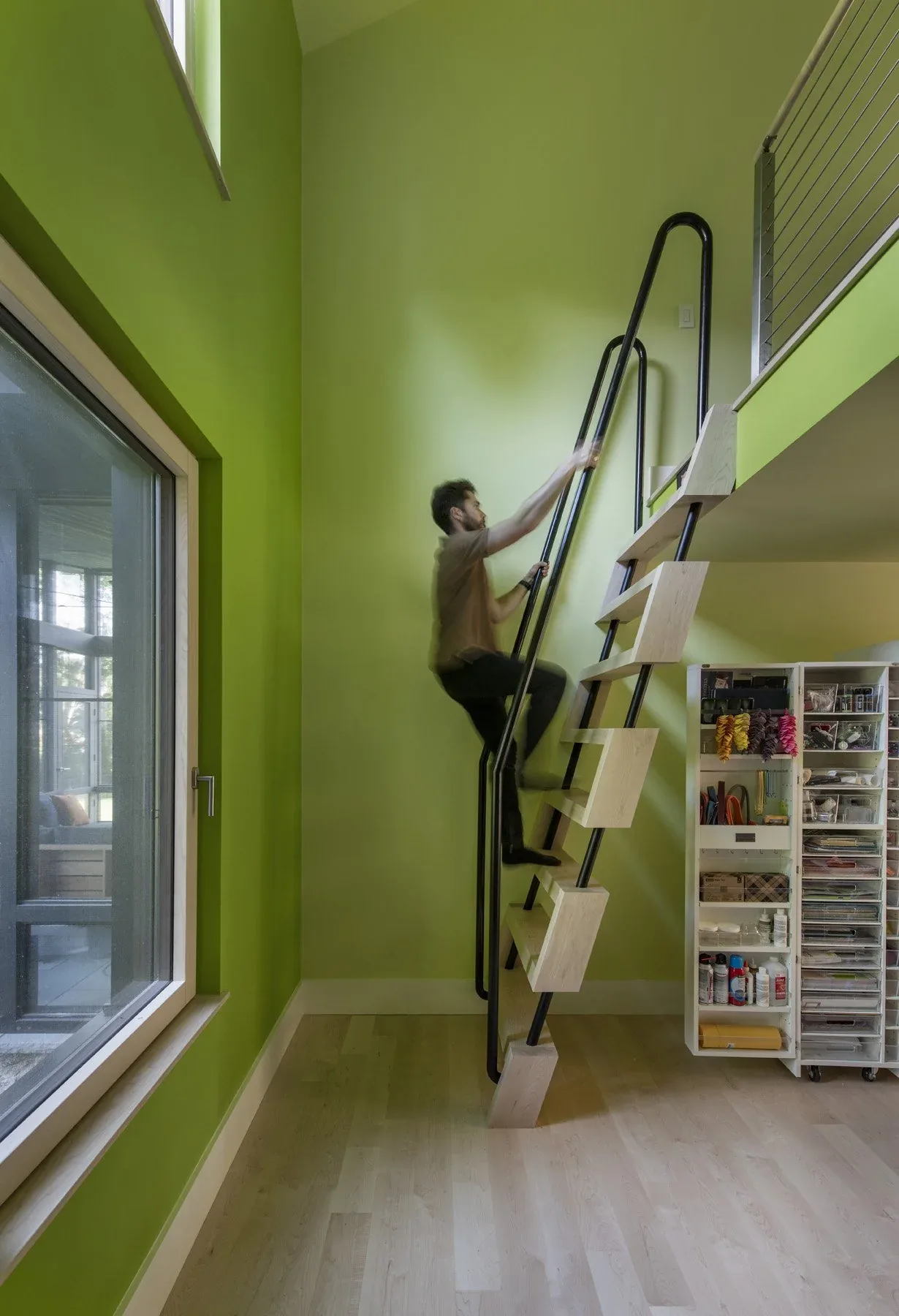 A compact staircase with light wood steps and black metal handrails ascends a wall painted in green inside a home.
