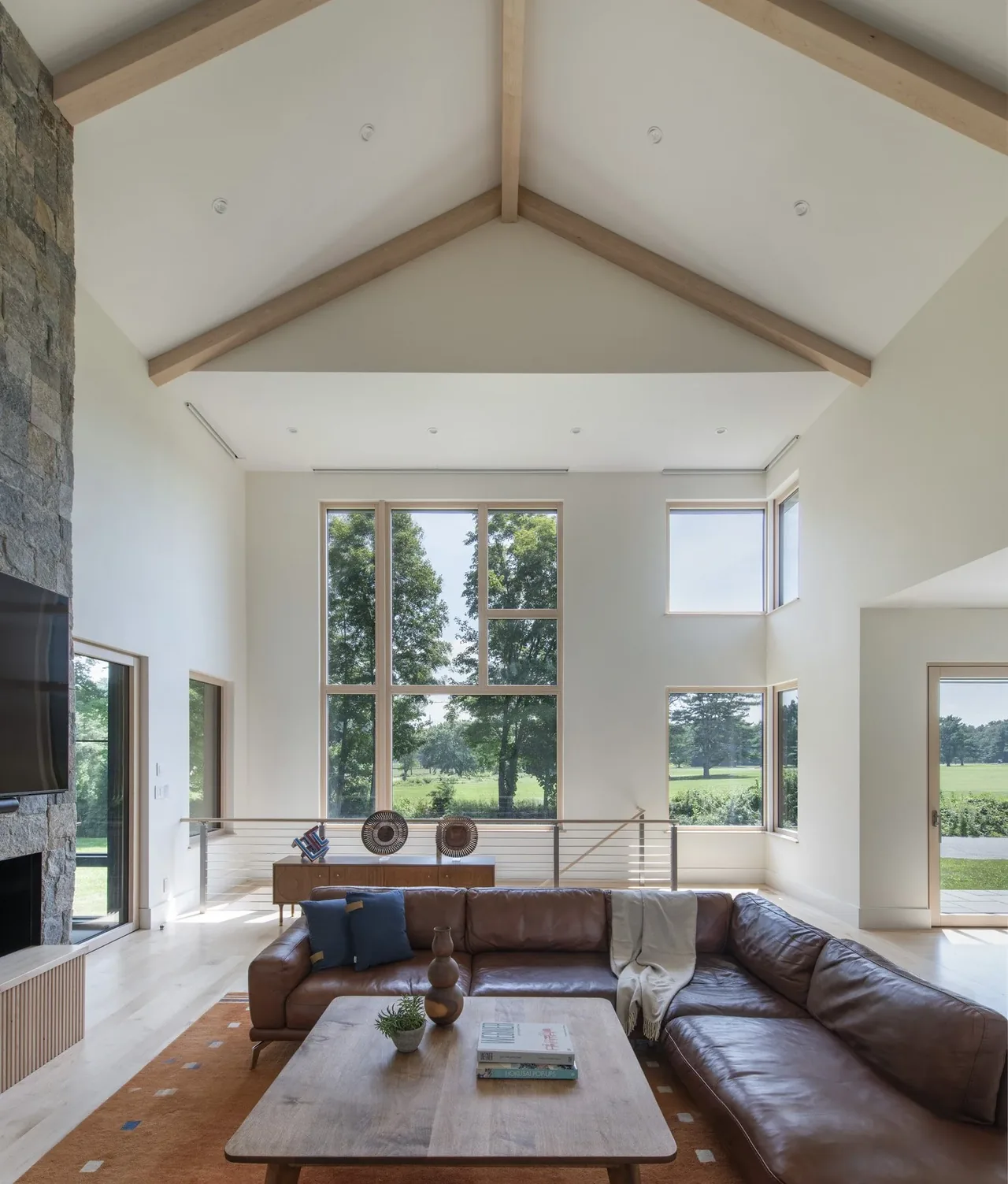 Living space in Stow Passive House features vaulted ceiling and expansive glazing with a view of the outdoor greenery.