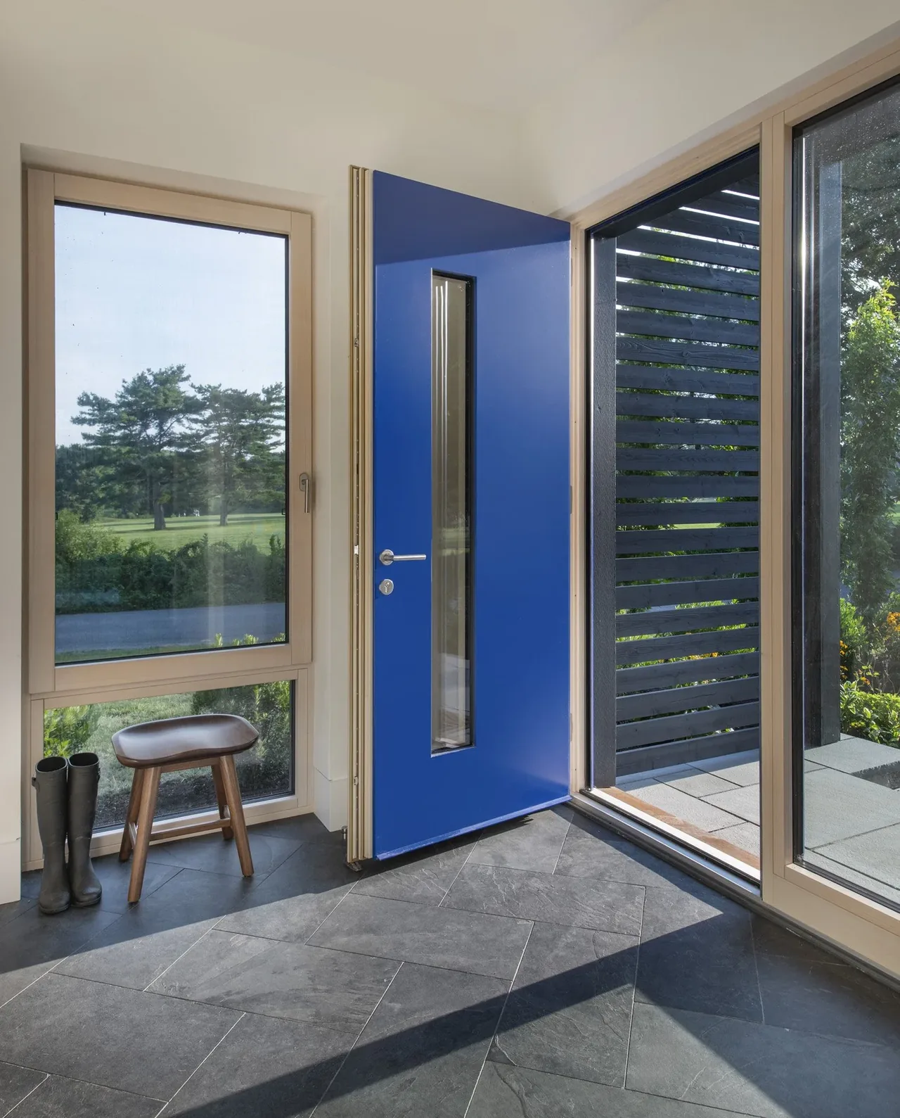 Entry area of Stow Passive House featuring a bold blue door and expansive glazing for natural views.