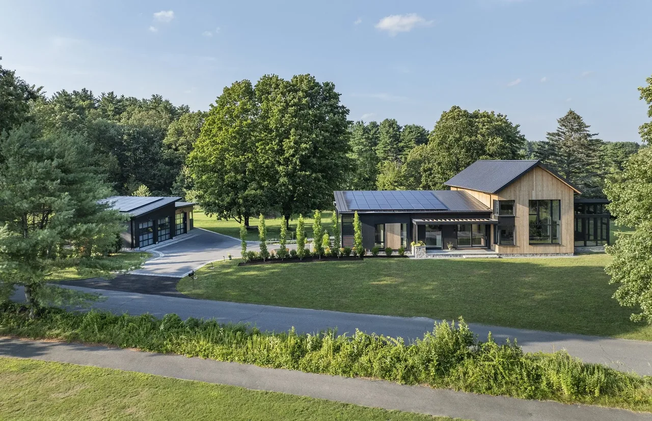 The Stow Passive House features timber cladding and dark metal roofs, set in a lush green setting with a detached garage.