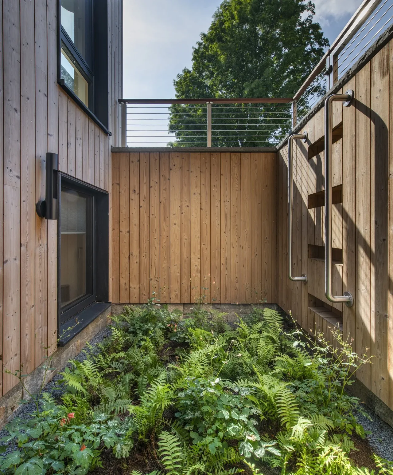 Wood-paneled exterior corner with a garden bed and metal handrails at Stow Passive House by ZeroEnergy Design.