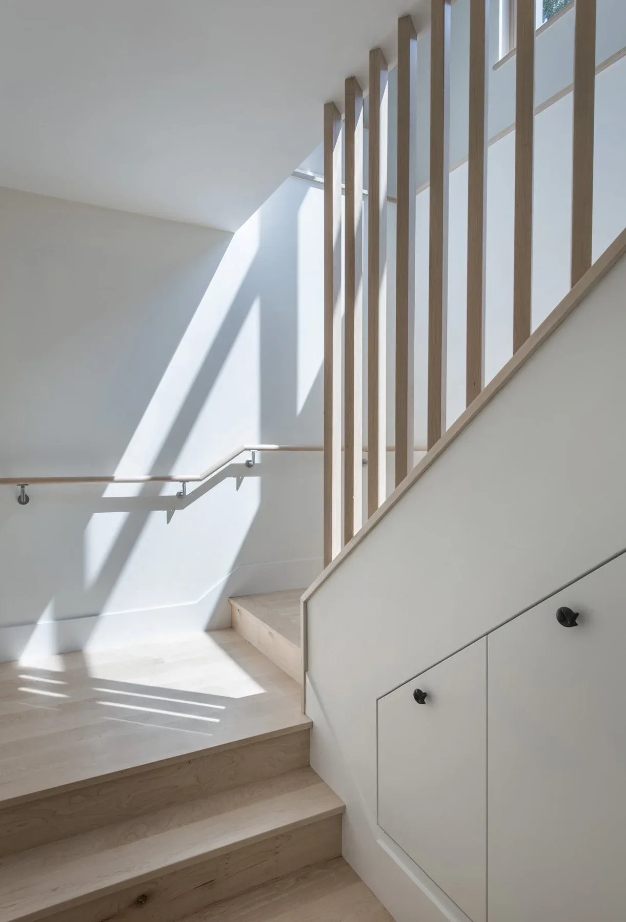 Minimalist stairwell featuring light wood steps and vertical wood slat railing illuminated by natural daylight.