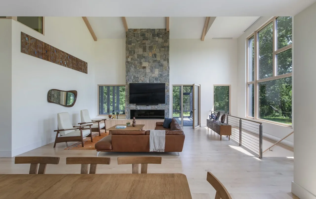 Spacious living room features a tall stone fireplace, leather seating, and expansive windows overlooking greenery.