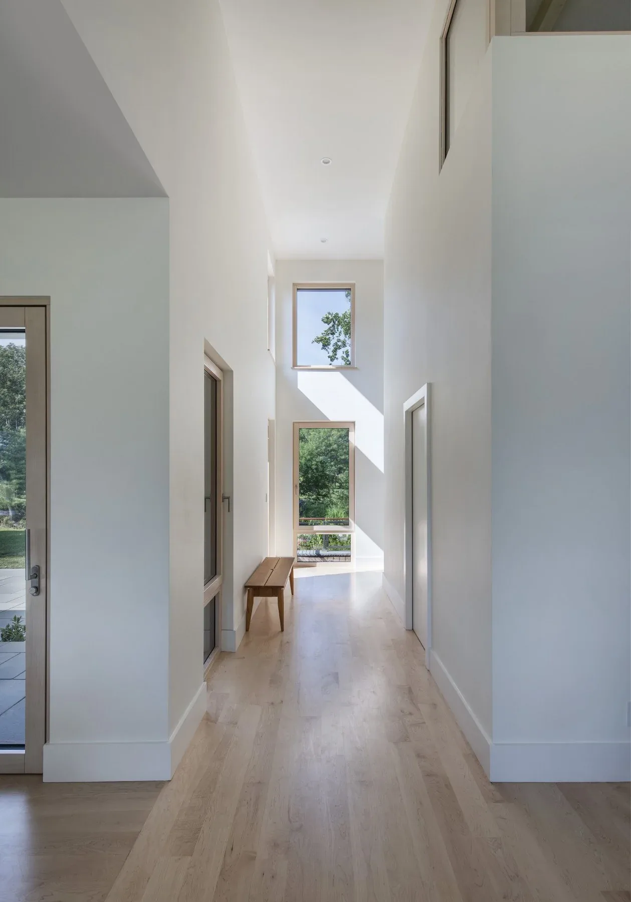 A high-ceiling hallway features light wood flooring and two vertically aligned windows.