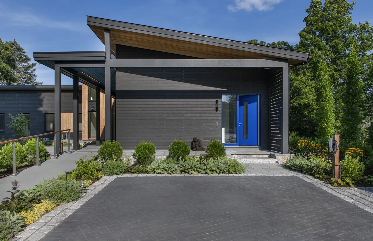 Modern home entrance features vertical wood siding, a blue door, and a covered porch with a sloped roof.