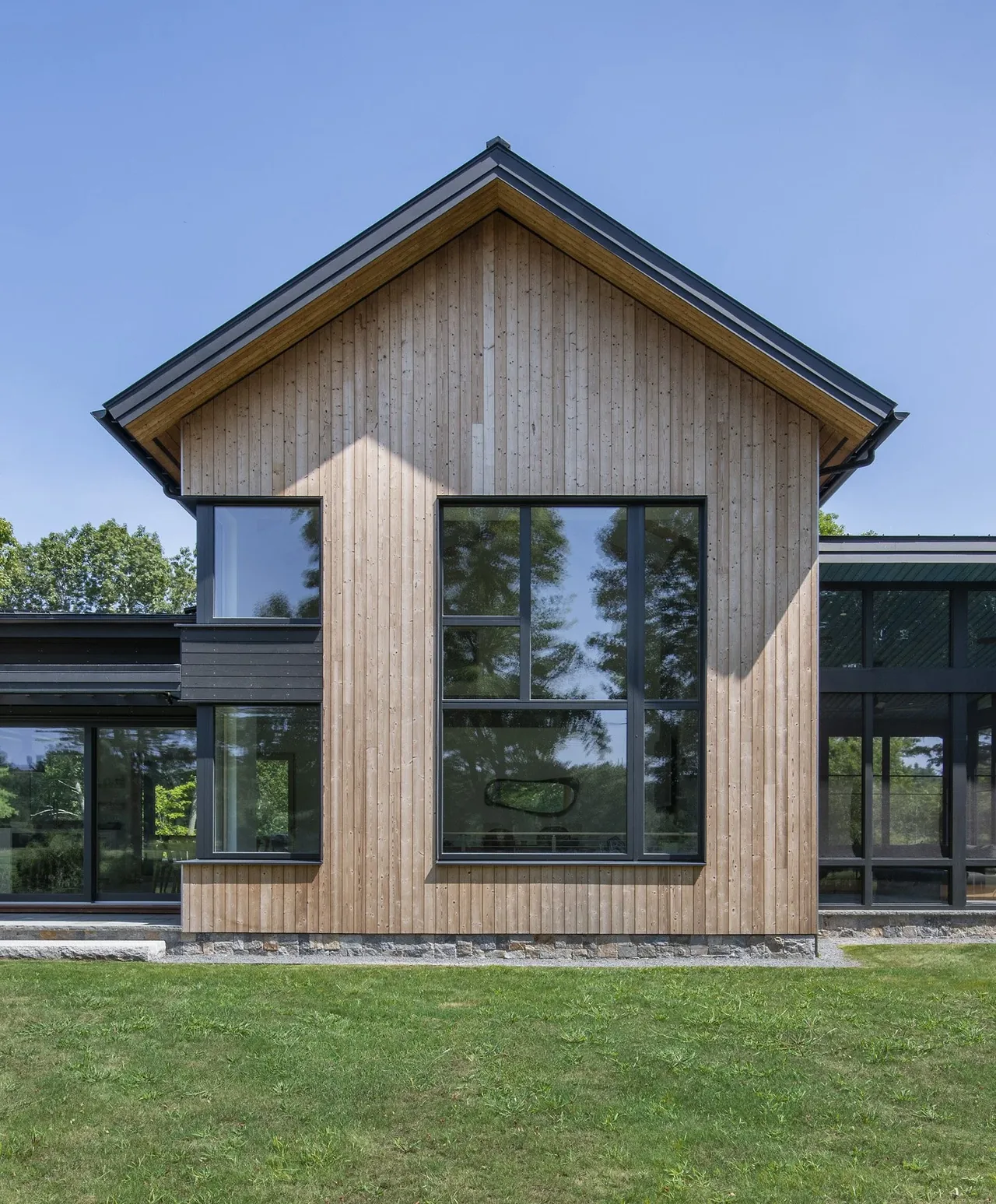 Stow Passive House features vertical wood siding and floor-to-ceiling black-framed windows under a gable roof.