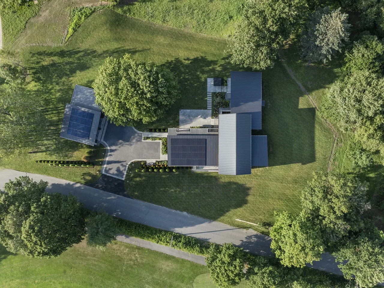 Stow Passive House features a detached garage and solar panels on the roof, situated in a landscaped grassy area with mature trees.