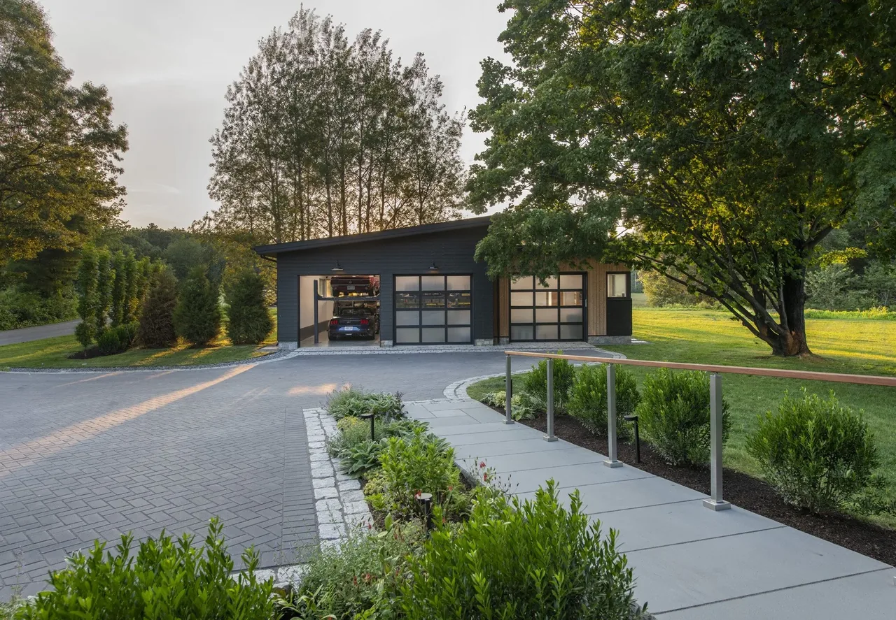 The detached garage features dark vertical wood siding and large glass panel doors, set within a landscaped yard.