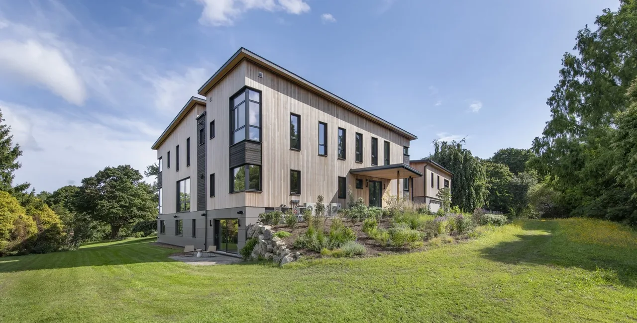 The Belmont Modern 2.0 features vertical wood siding, large windows with black frames, and a landscaped sloped side yard.