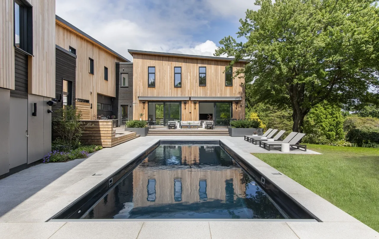 Modern two-story home with wood siding, large vertical windows, and a rectangular pool with surrounding seating area.
