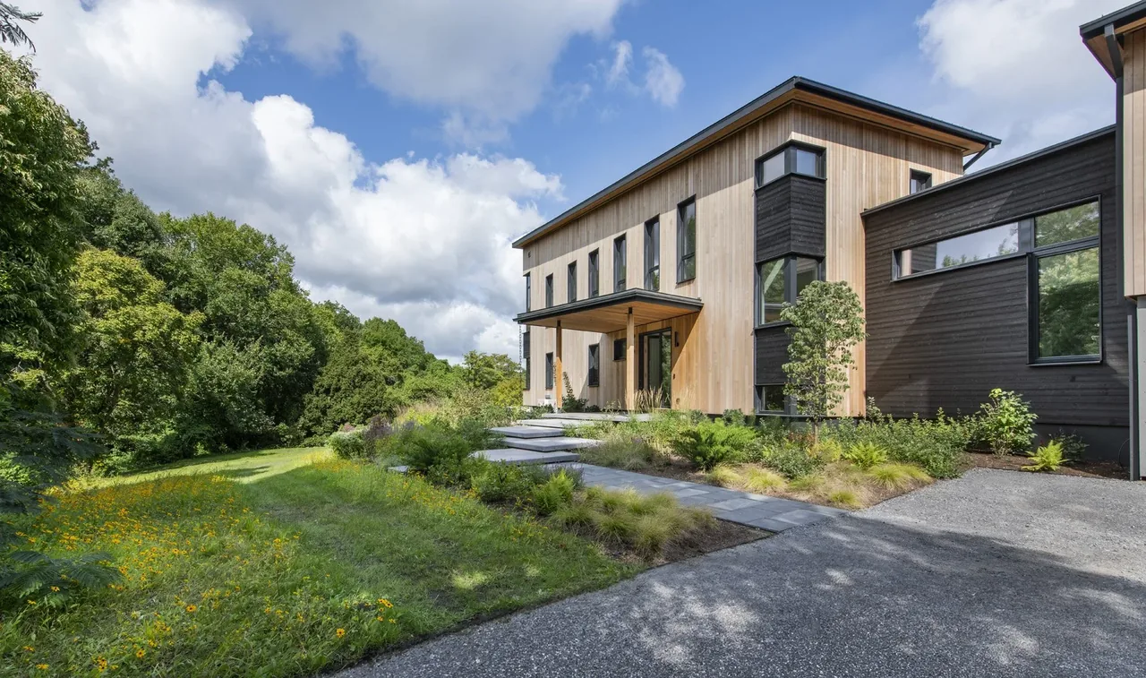 Modern two-story home featuring wood siding, black window frames, and a landscaped front yard with stone steps.