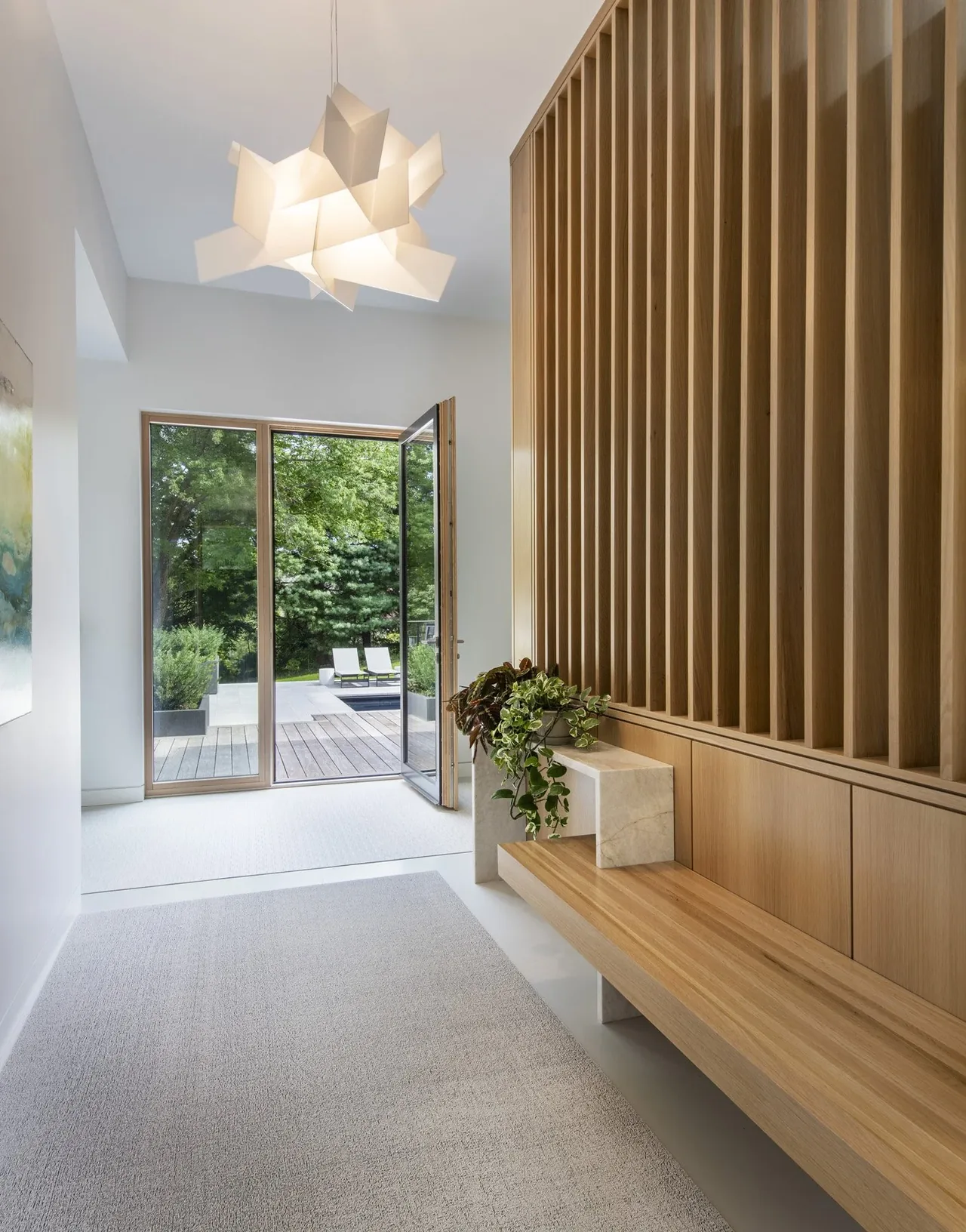 Entryway of Belmont Modern 2.0 features wood slat wall, a contemporary pendant light, and glass doors to the outdoor deck.
