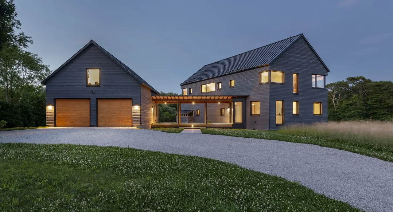 Westport Modern Home features dark wood siding, a double garage with wood doors, and a connecting pergola breezeway under a gable roof.