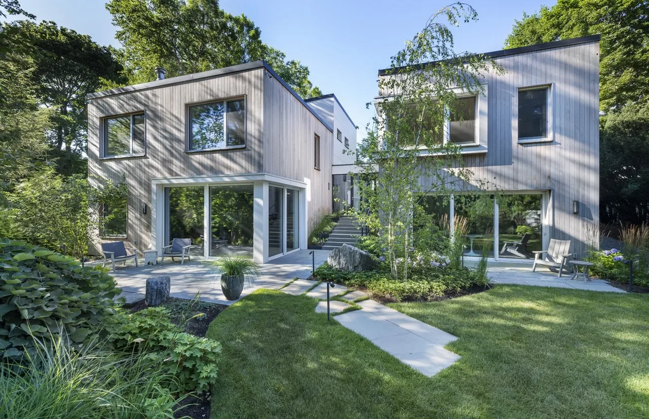 The exterior view of Belmont Modern showcases a two-story home with light wood siding, large sliding glass doors, and a landscaped yard.