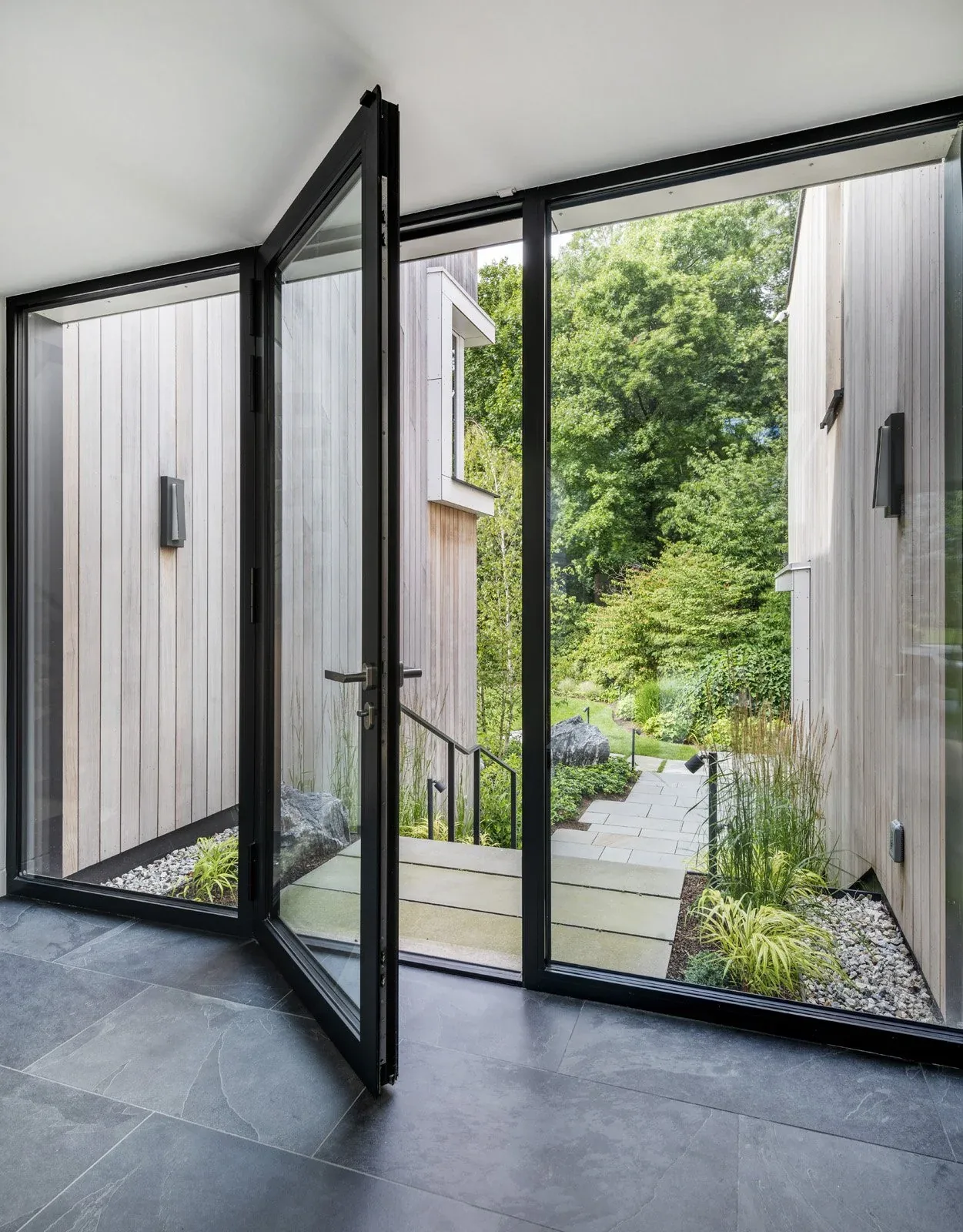 The open glass door with black frames connects interior space to landscaped outdoor path and garden area.