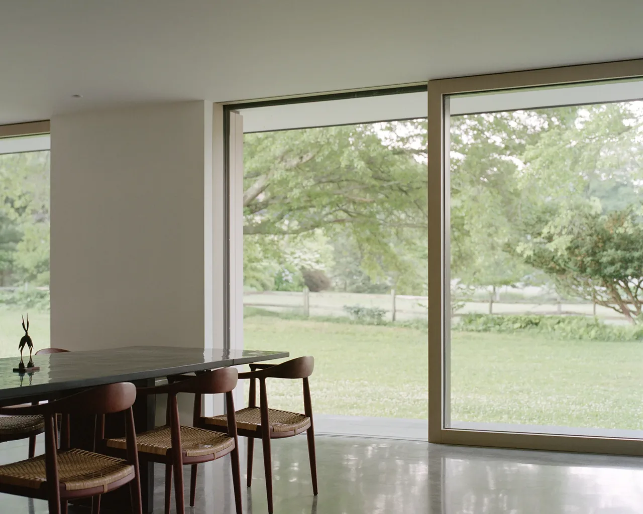 The Berkshire Residence features an interior dining area with floor-to-ceiling glazing that overlooks a green meadow.
