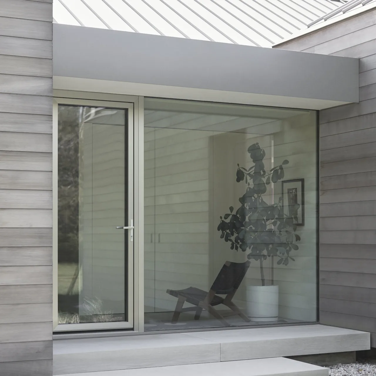 The glass door and picture window in a wood-sided section of the East Hampton Residence show a modern design with outdoor concrete steps.