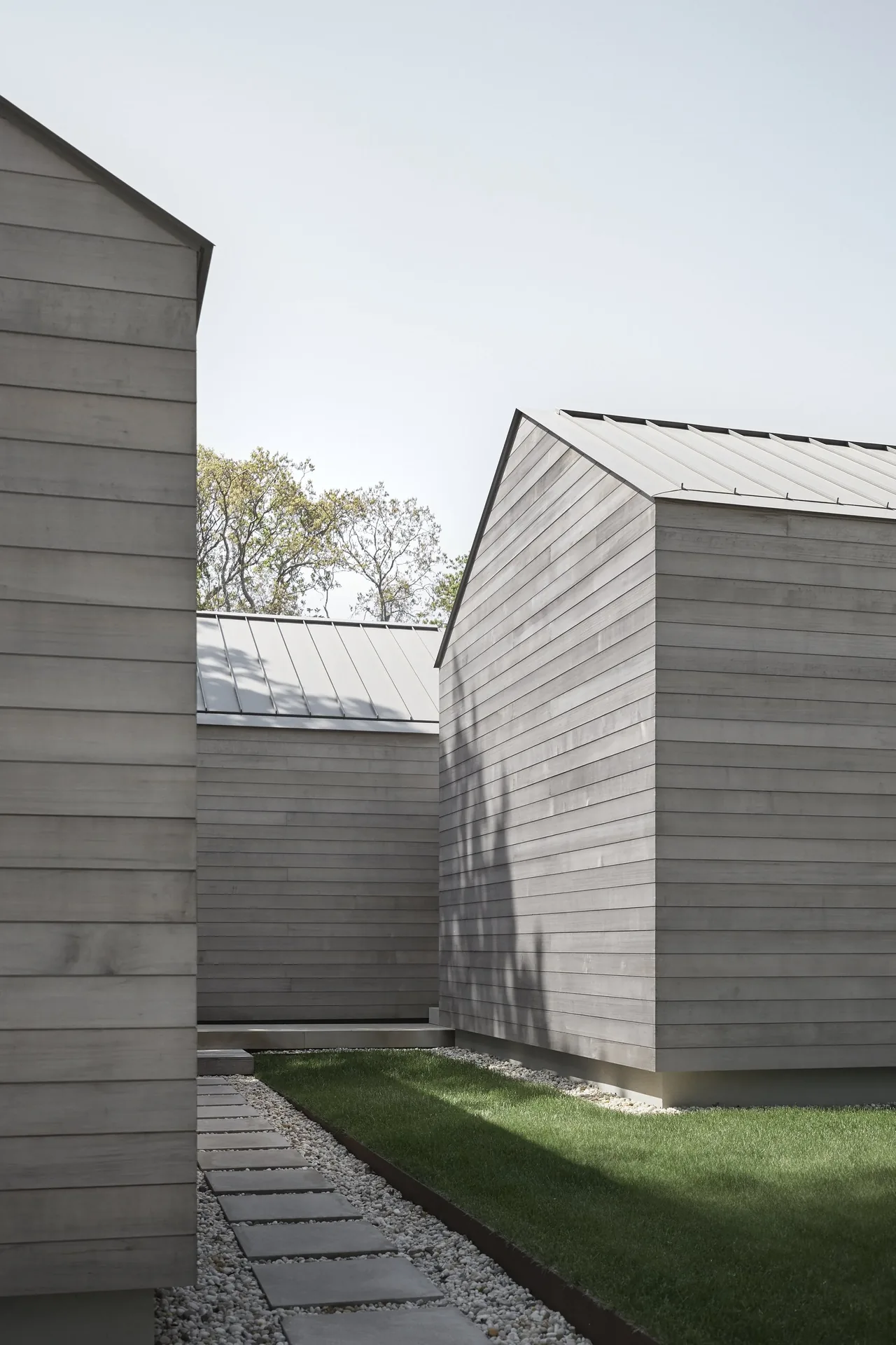 East Hampton Residence features rectangular building wings clad in horizontal siding with metal gable roofs.
