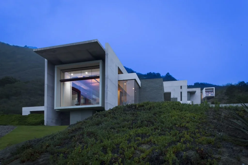 Hilltop modern house features large floor-to-ceiling glazing and prominent rectangular concrete frame volumes.