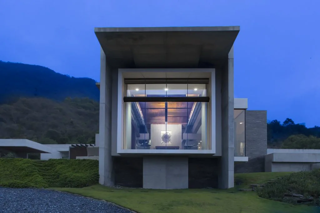 Exterior view of modern house featuring a large cantilevered concrete frame and expansive glazing with mountain backdrop.