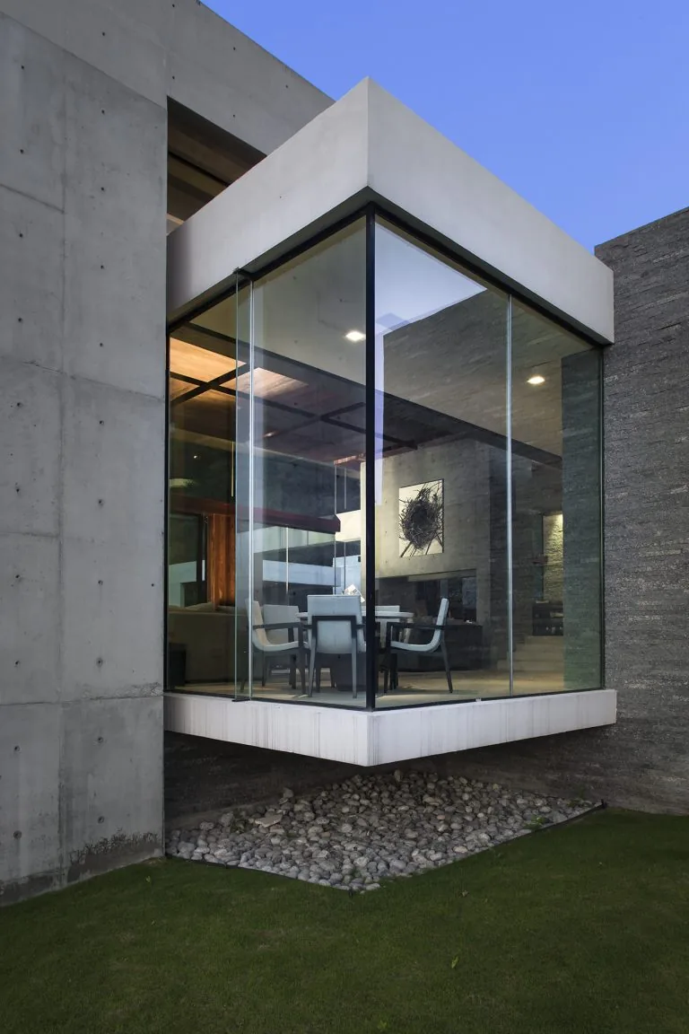 The house features a cantilevered glass-walled dining room corner with a concrete exterior and pebble landscaping beneath.