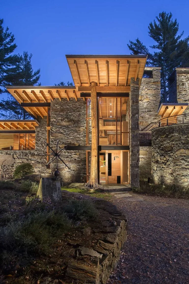 Night view of house entrance showing stone retaining walls and exposed wood beams under flat roofs.