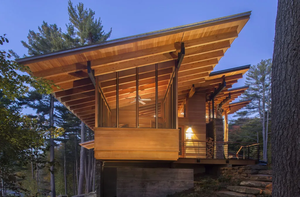 House in the Berkshires features exposed wood beams and large windows in a rural forest environment.