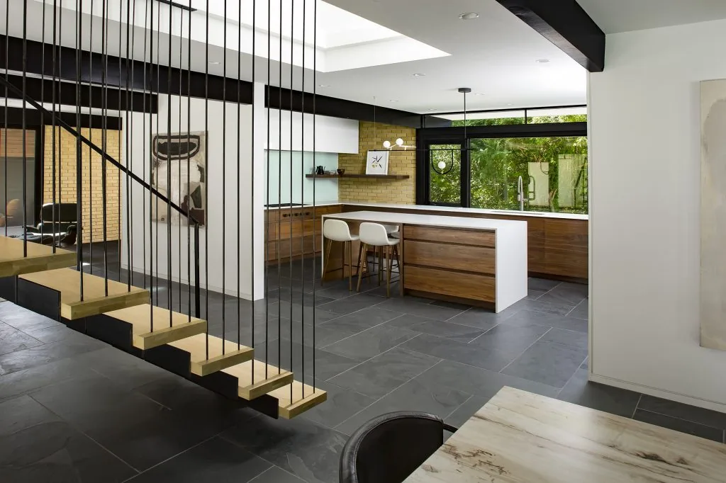 Kitchen and adjacent living space feature cantilevered wood stairs and black window frames with a view of the outdoors.