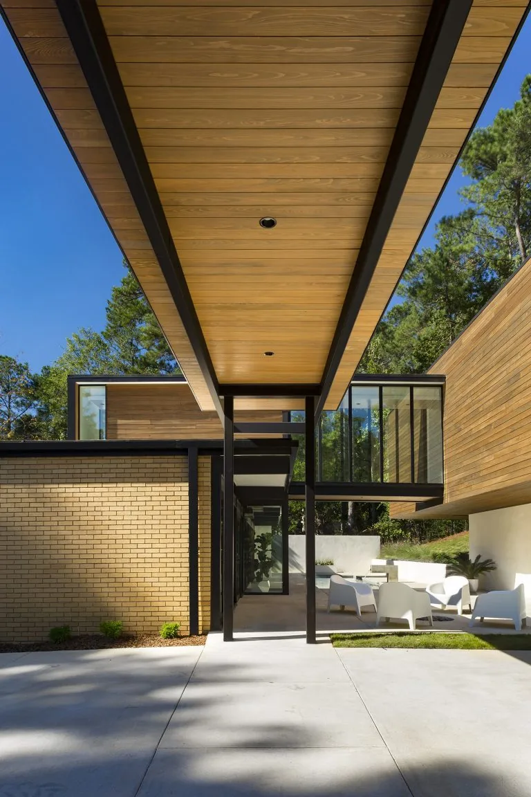 House in Mountain Brook with cantilevered second floor, wood siding, and outdoor seating area under a covered patio.