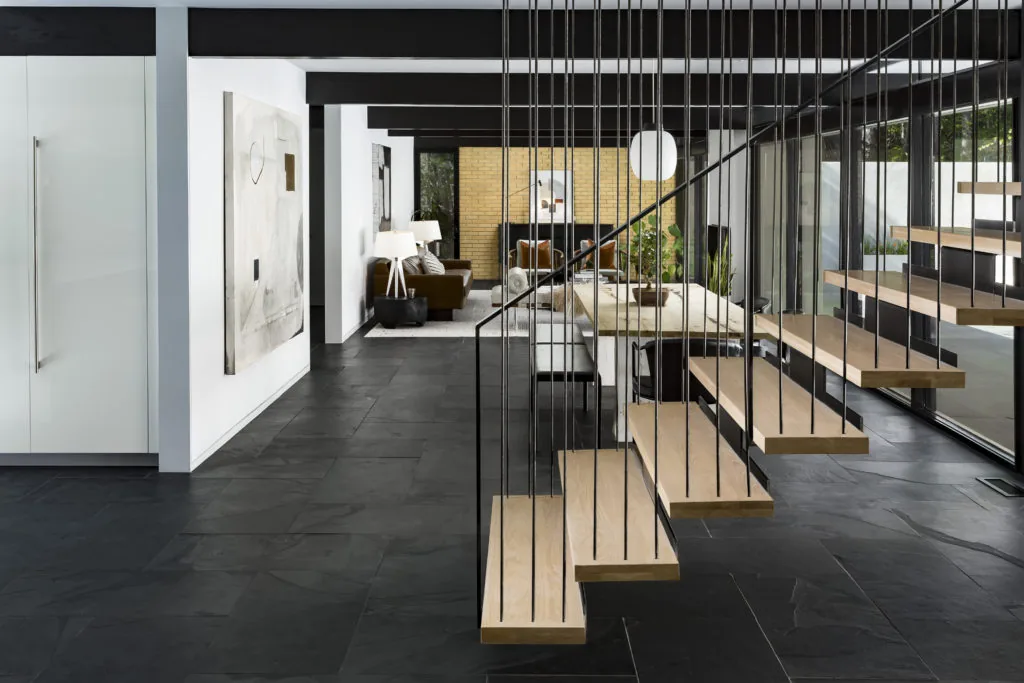 The House in Mountain Brook features floating wood stairs with suspended cables, black slate flooring, and expansive windows providing natural light.