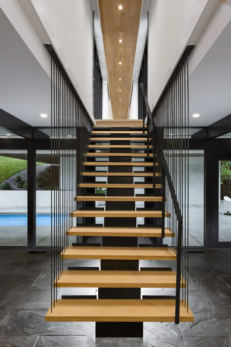 Modern floating staircase with suspended wood steps and black metal cables in a bright entry space.