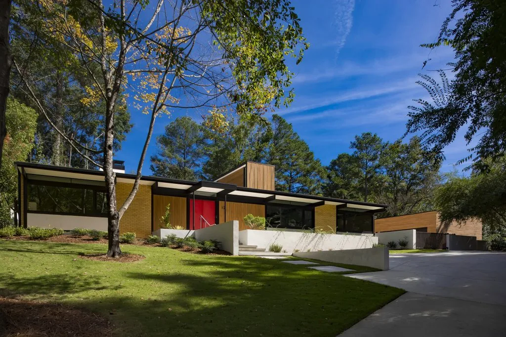 House in Mountain Brook features yellow brick walls, black window frames, wood siding, and a bright red front door.
