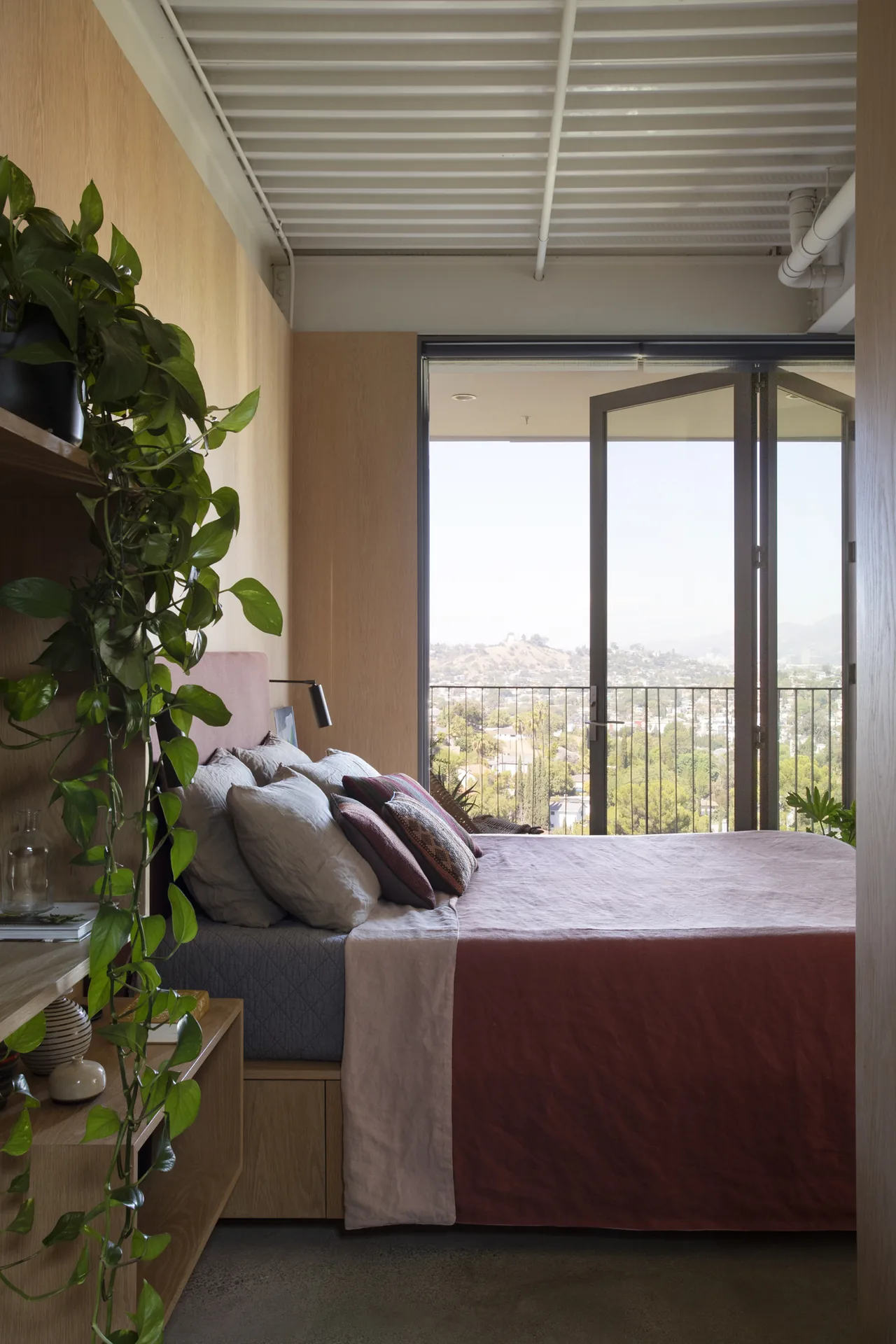 Olancha House bedroom features wood paneled walls and a balcony with city views.