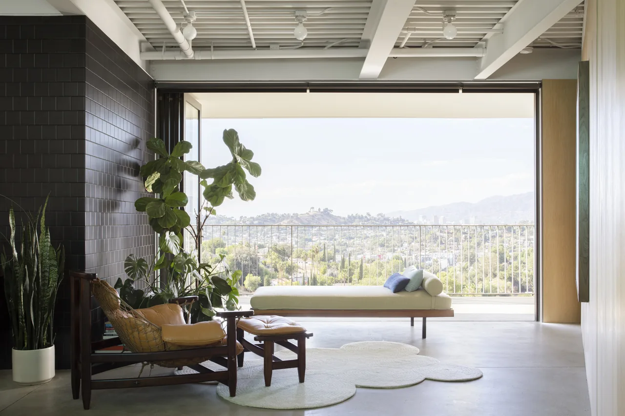 Living room in Olancha House with black subway tile wall, leather sling chair, and city view in Los Angeles.