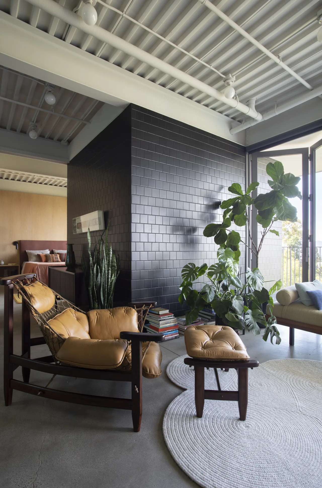 Living area of Olancha House features a leather sling chair and black subway tile wall with indoor plants near an open sliding glass door.