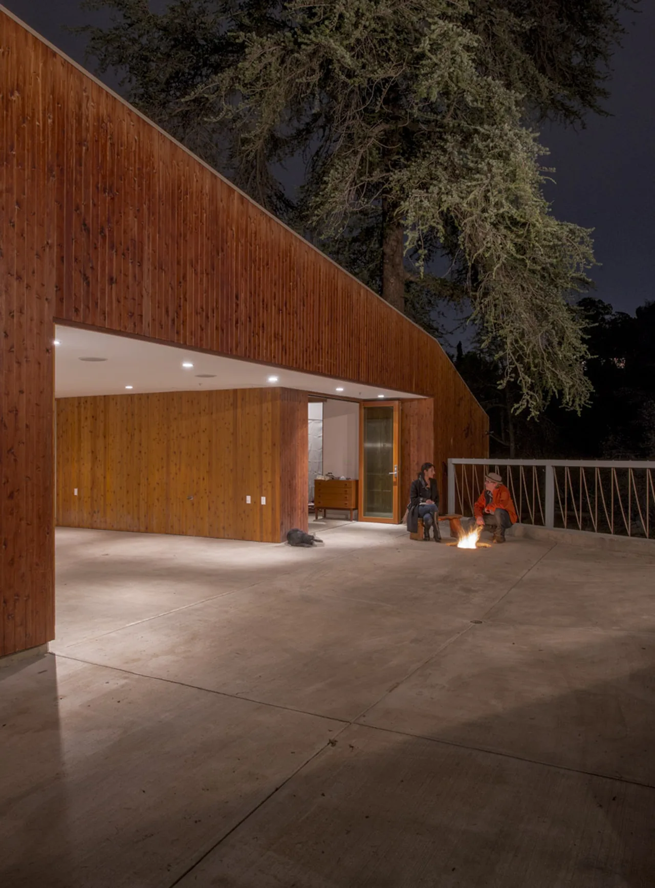 This modern hilltop home features a wood exterior and a concrete patio illuminated at night by recessed lighting.