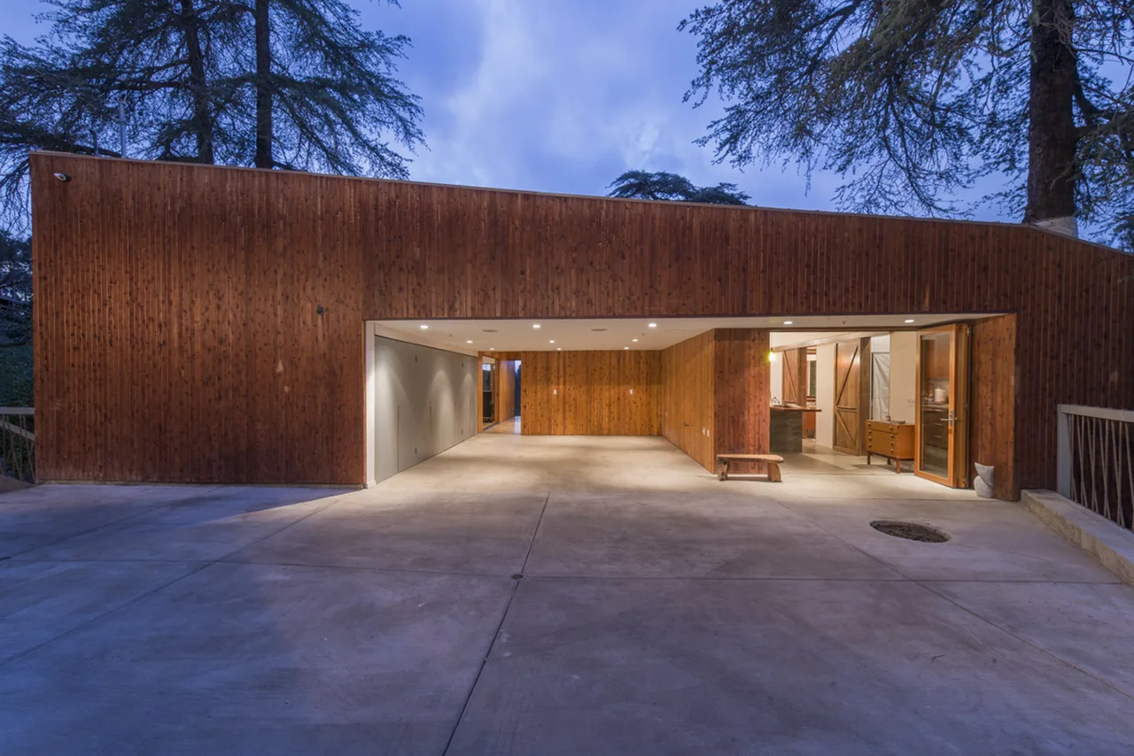 Modern wood-paneled garage and adjacent house entry lit at dusk with concrete driveway and large opening.