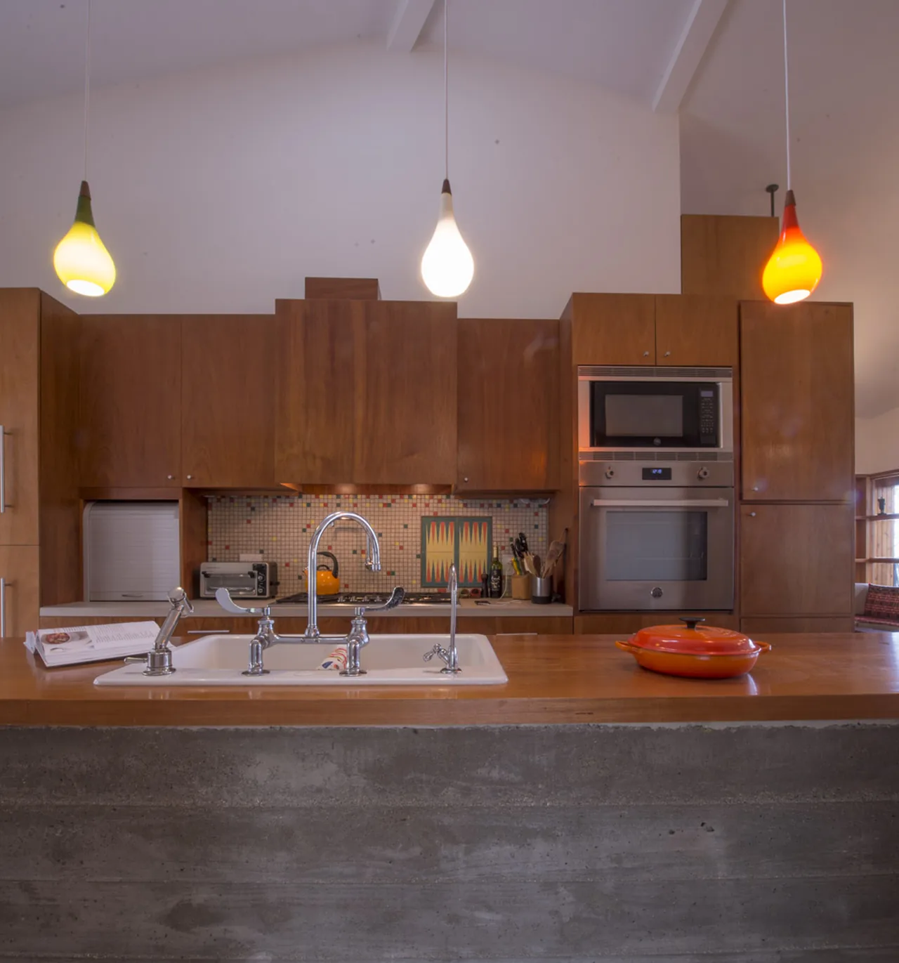 Modern kitchen with wood cabinets, mosaic tile backsplash, and a concrete island base under pendant lighting.