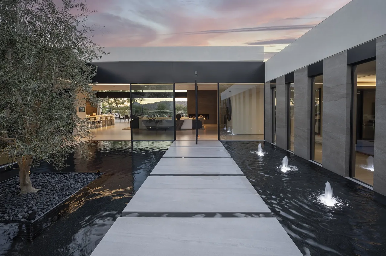 Concrete stepping stone path crosses a reflecting pool with fountains in the courtyard of a modern home at sunset.