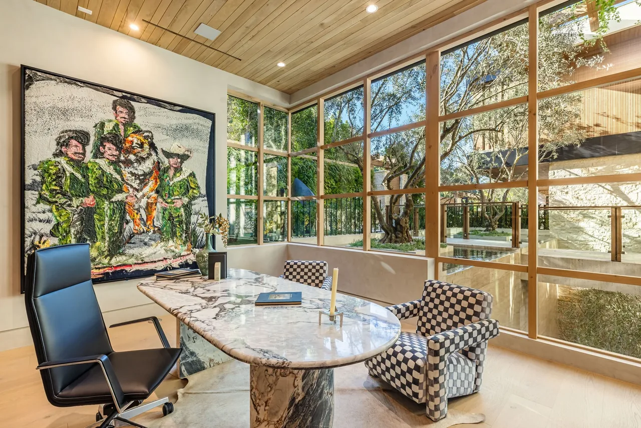 Modern office with a marble desk and corner windows overlooking an outdoor courtyard with trees and glass railing.