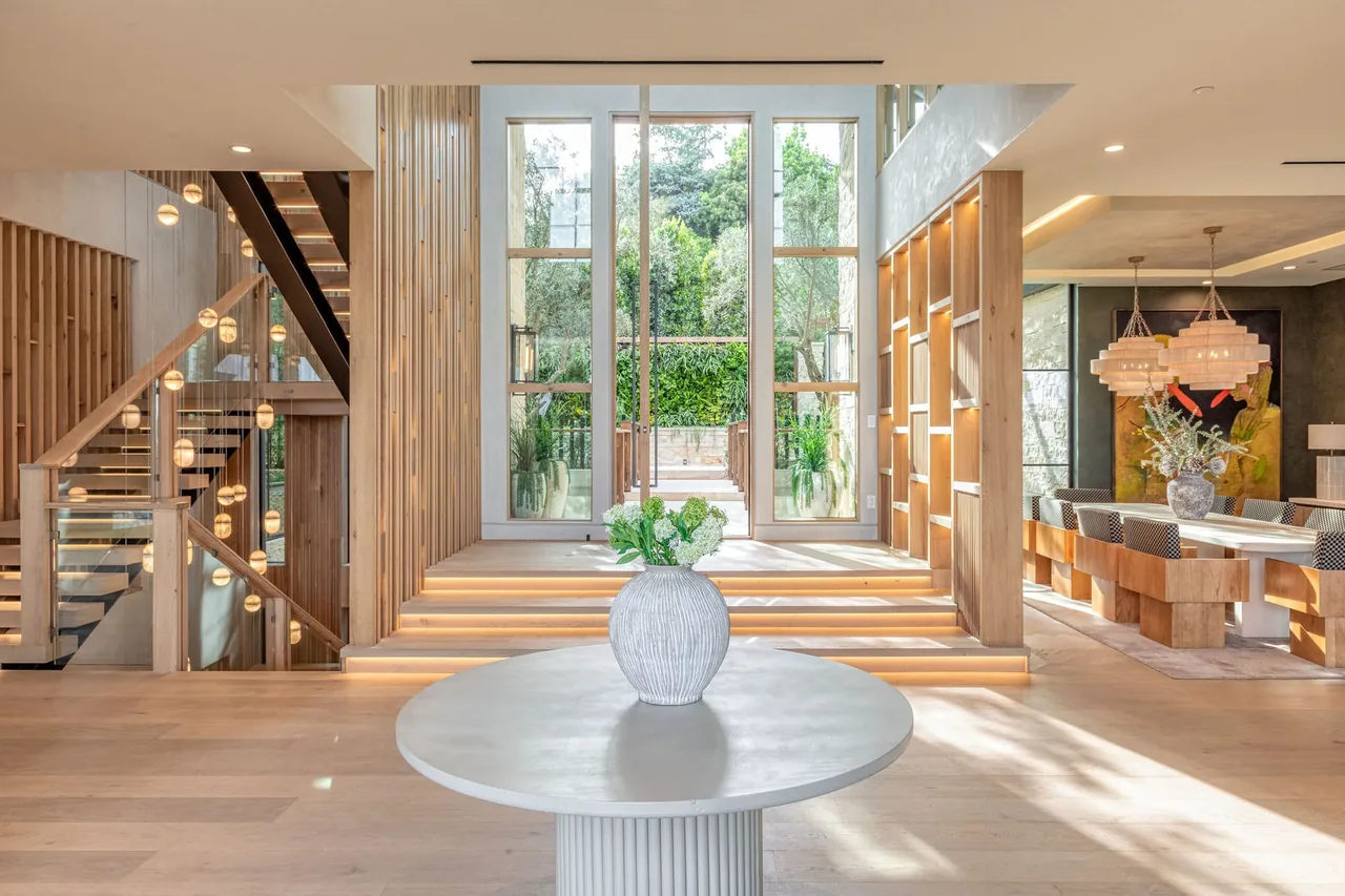 Open living and dining area features floor-to-ceiling windows, wood wall panels, and built-in shelving with pendant lights over the dining table.